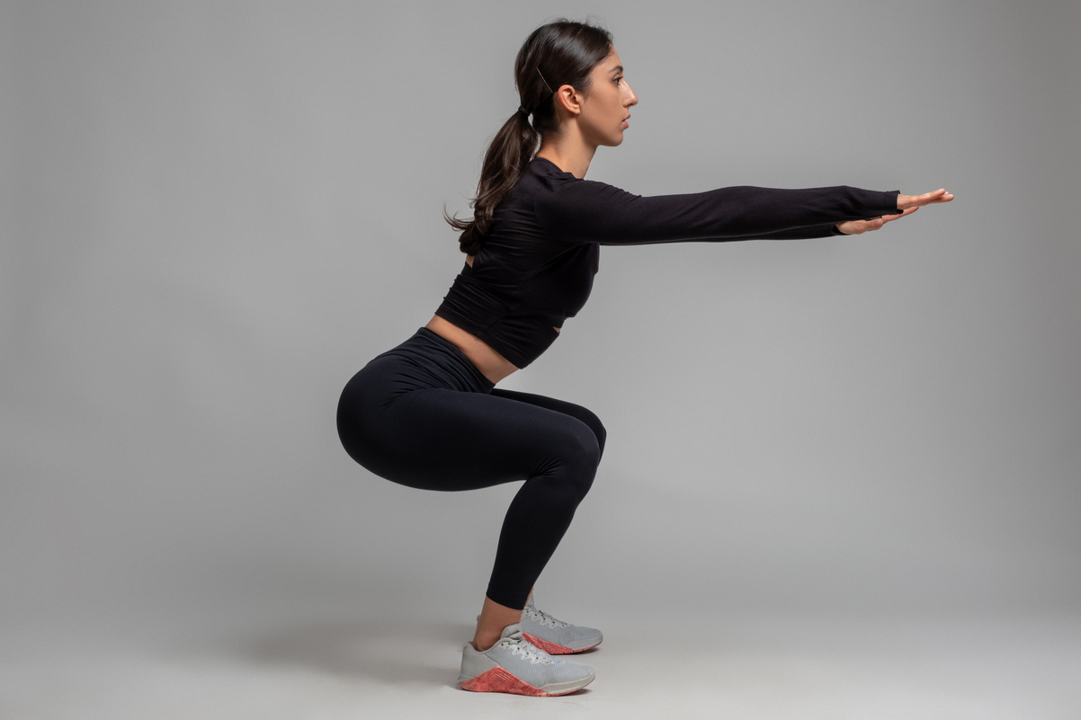 Side View of Girl Doing Squats on Grey Background